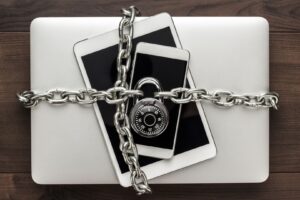 Celular, tablet e notebook presos por uma corrente e cadeado representando segurança.