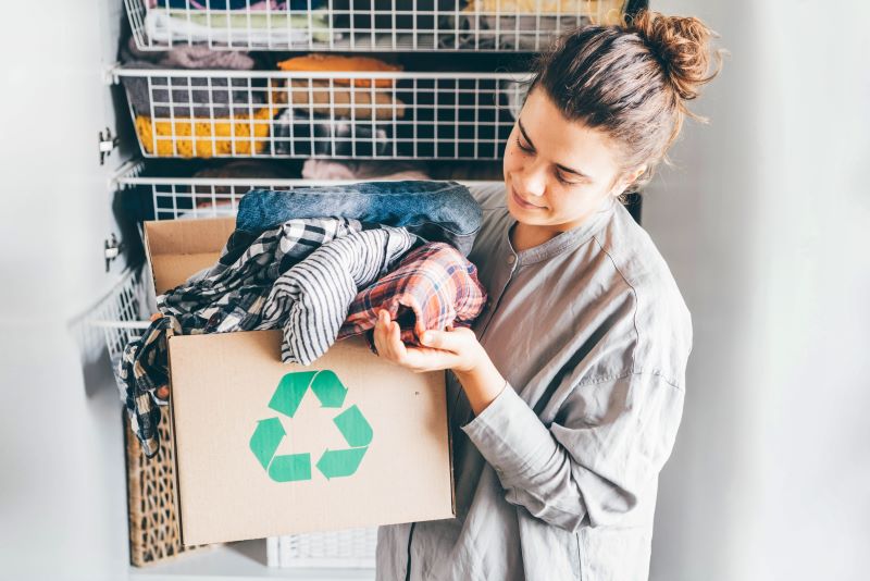 Mulher segurando uma caixa de roupas. A caixa possui um símbolo de material reciclável.